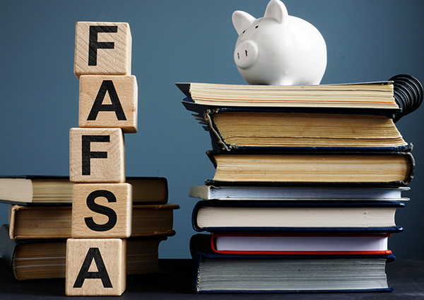 wood blocks spelling FAFSA  and piggy bank on top of book pile